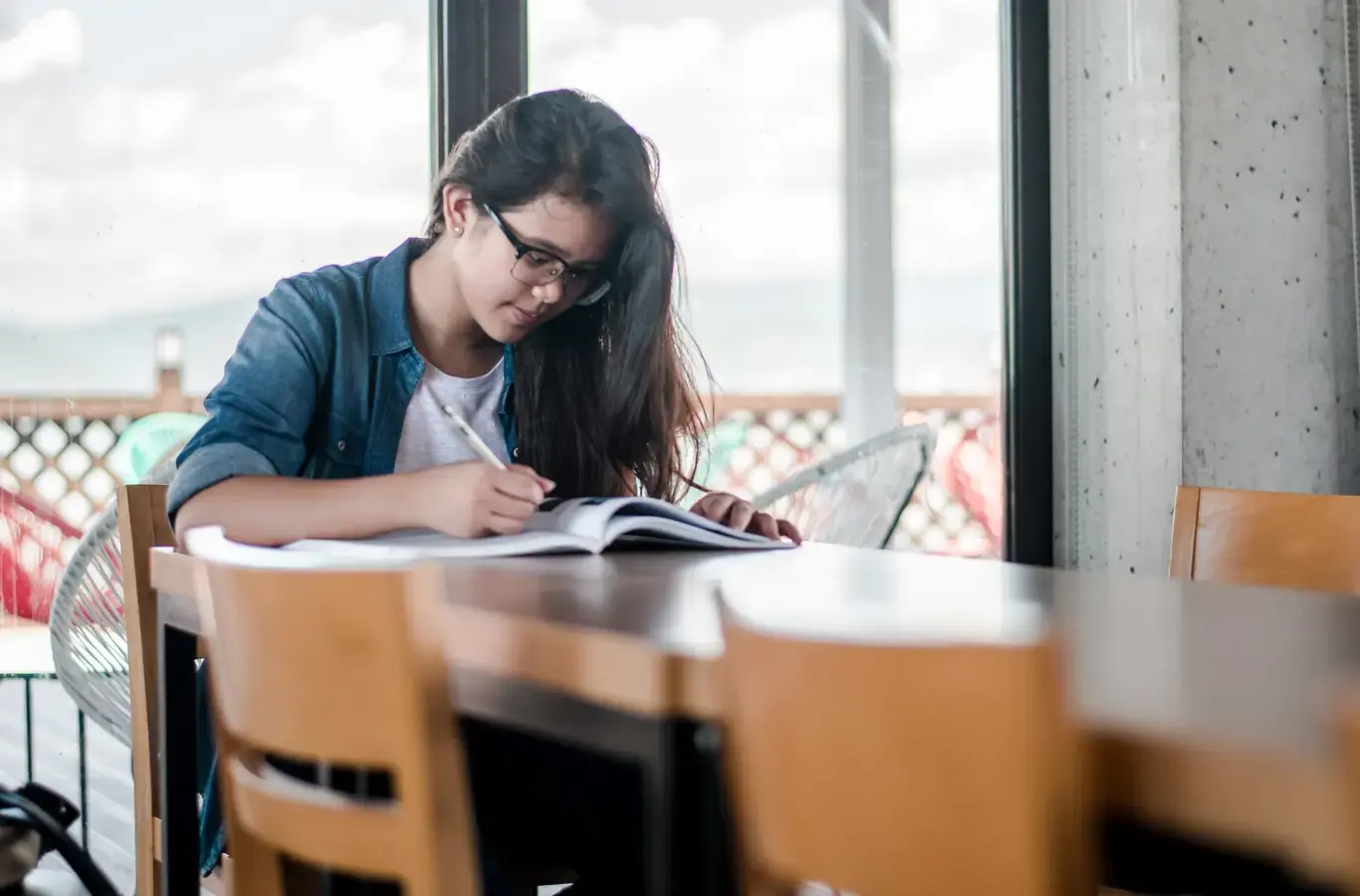 menina usando óculos e estudando apoiada em uma mesa para ilustrar o conteúdo sobre quanto vale cada questão do enem