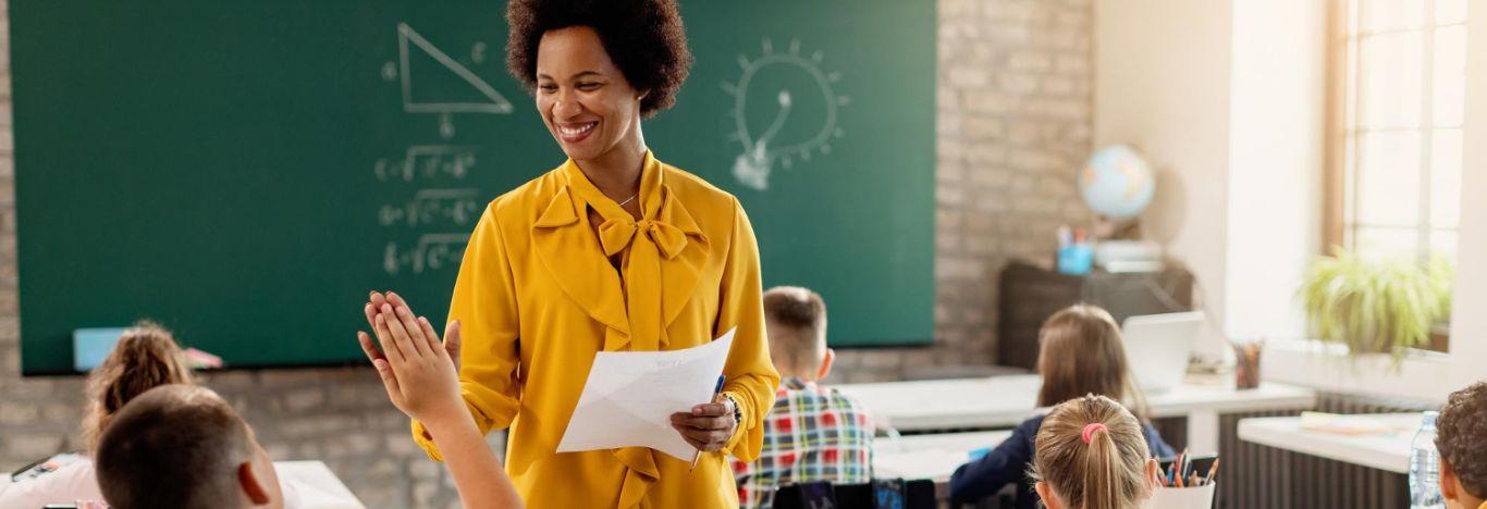 professora segurando uma olha e olhando para o aluno para ilustrar o conteúdo sobre matérias para concurso de pedagogia