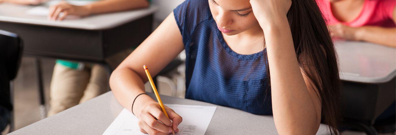 Uma pessoa escrevendo no caderno, em uma sala de Aula